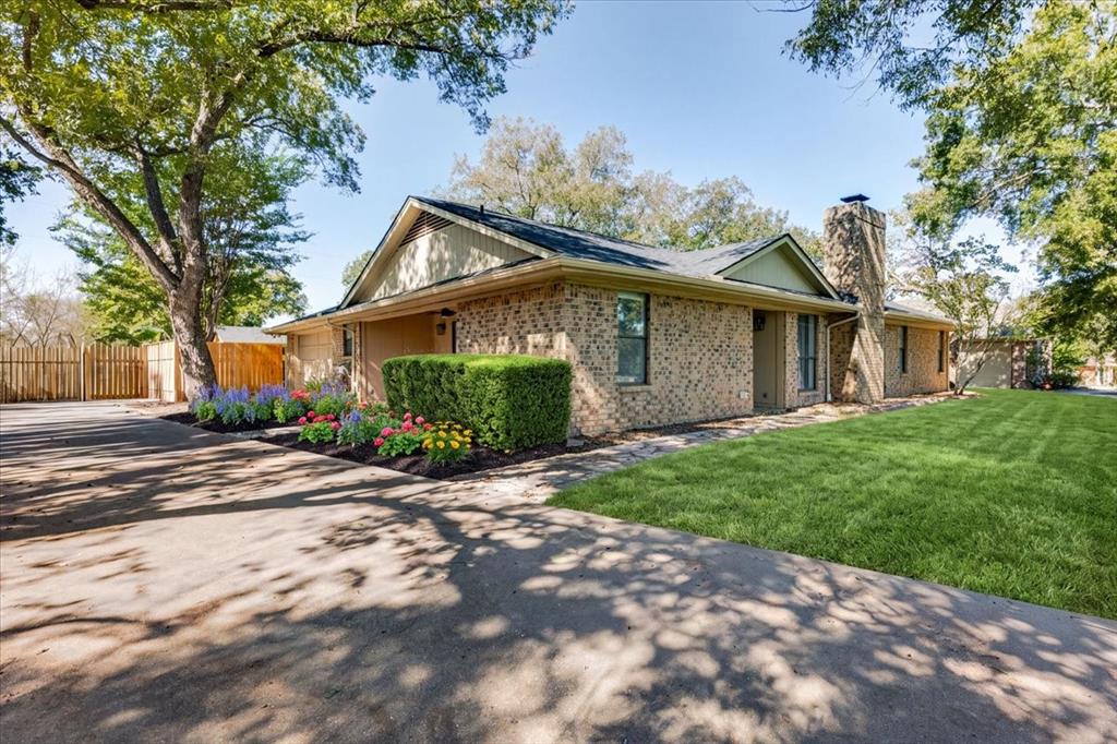8105 Ravenswood Road Granbury, TX 76049 - Photo 1 of 28 Brick exterior with a prominent stone chimney, established trees, vibrant landscaping, and a well-maintained lawn