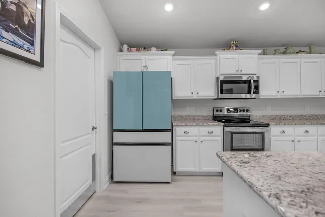 a kitchen with granite countertop a refrigerator stove and white cabinets