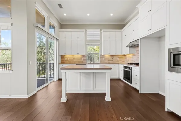a kitchen with stainless steel appliances granite countertop a refrigerator a stove a sink and white cabinets with wooden floor next to windows