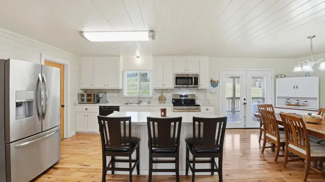 a kitchen with stainless steel appliances granite countertop a stove top oven a refrigerator a sink and a dining table with wooden floor