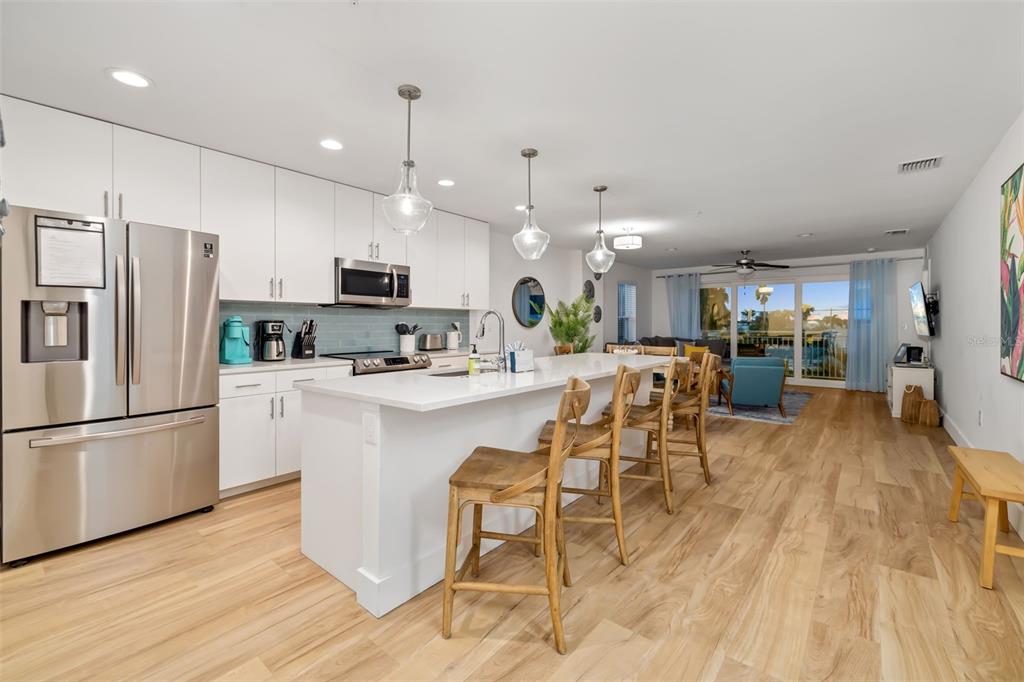 15305 1st Street East, Unit 201 Madeira Beach, FL 33708 - Photo 19 of 41 a kitchen with stainless steel appliances kitchen island granite countertop a refrigerator a stove a sink a dining table and chairs with wooden floor