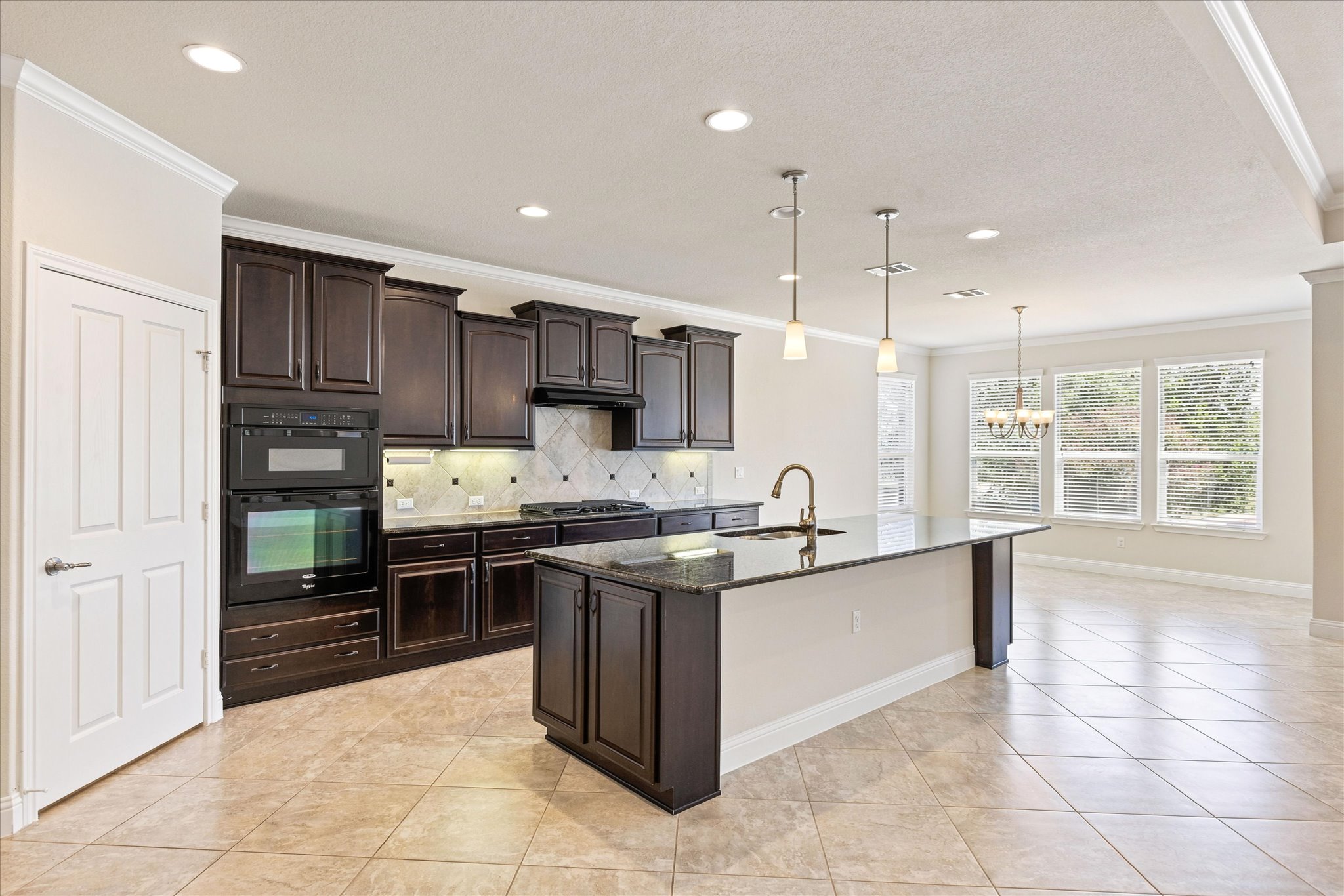 Rich dark cabinetry and a central island ground this open-concept kitchen with tile flooring.