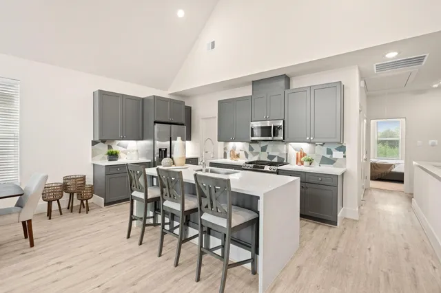 a dining hall with stainless steel appliances granite countertop a sink a stove a dining table and chairs with wooden floor