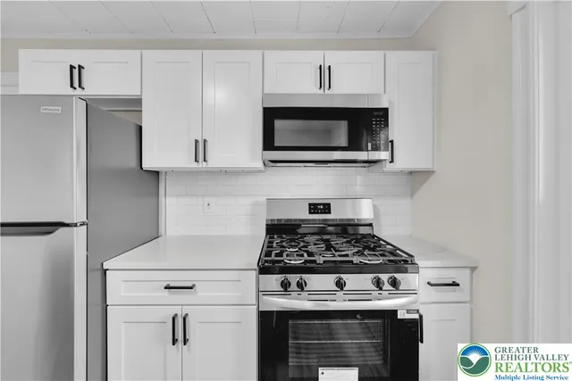 a kitchen with stainless steel appliances granite countertop white cabinets a stove a microwave and a refrigerator