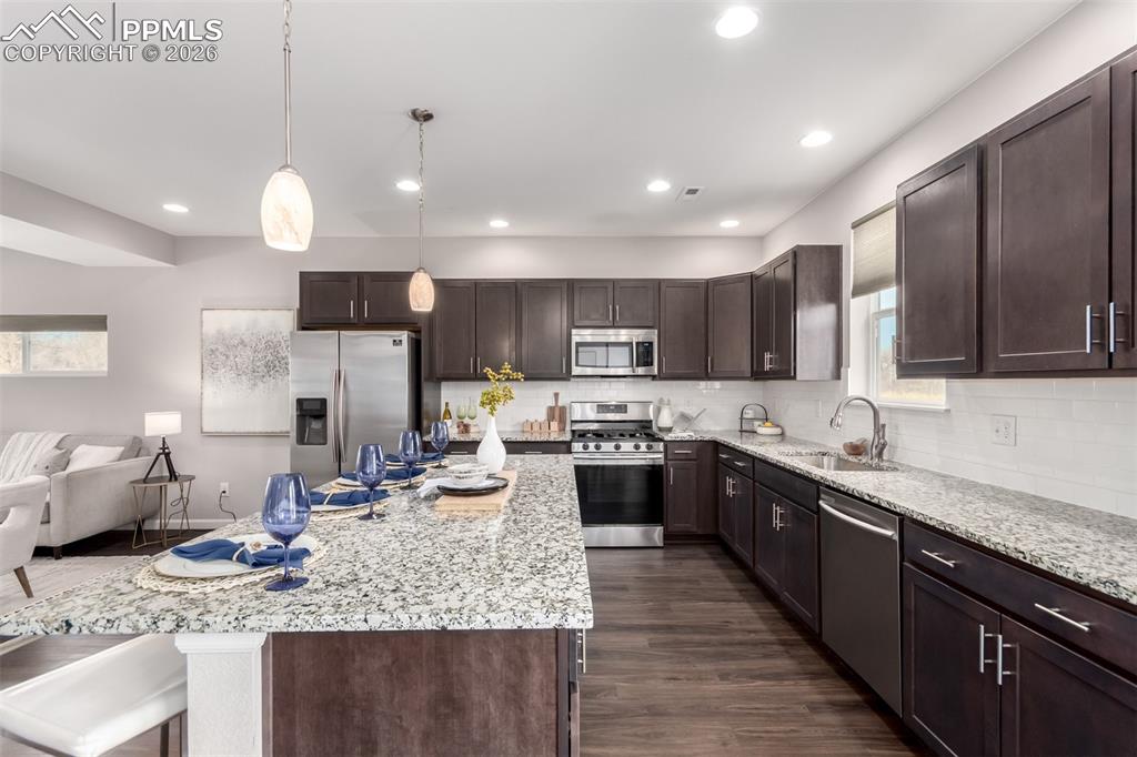 7956 Osage Street Denver, CO 80221 - Photo 12 of 48 Kitchen featuring dark brown cabinets, stainless steel appliances, decorative light fixtures, light stone counters, and dark wood-type flooring