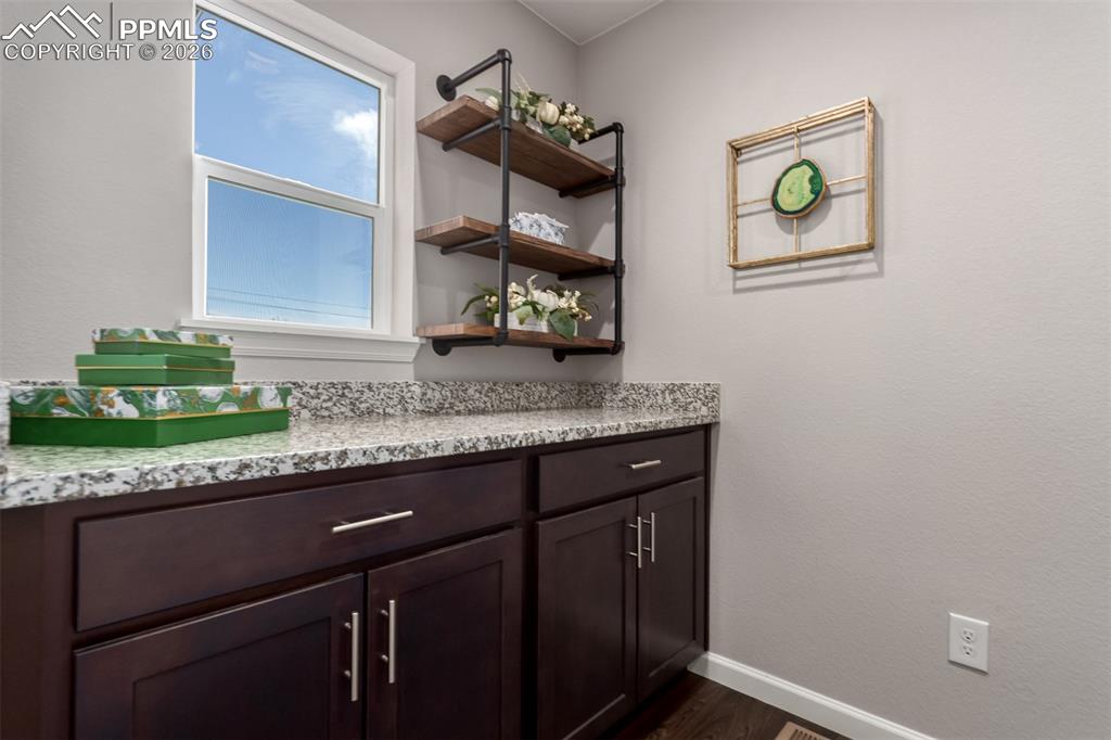 7956 Osage Street Denver, CO 80221 - Photo 30 of 48 Bar area featuring open shelves, dark brown cabinetry, light stone counters, and dark wood-type flooring