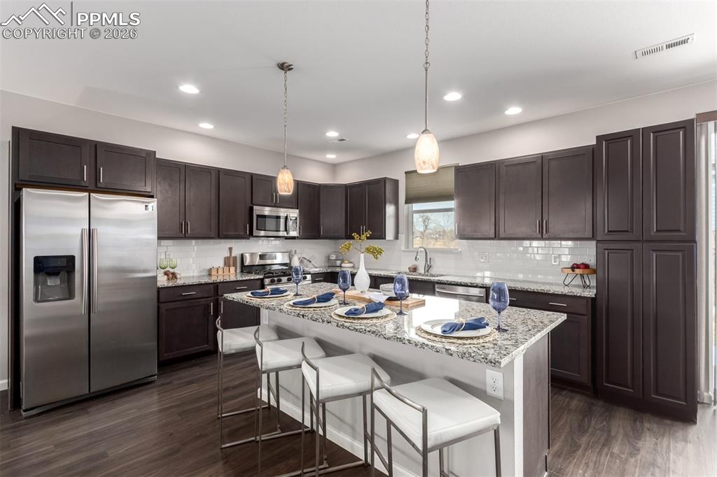 7956 Osage Street Denver, CO 80221 - Photo 10 of 48 Kitchen with stainless steel appliances, a breakfast bar, light stone counters, decorative light fixtures, and dark brown cabinetry