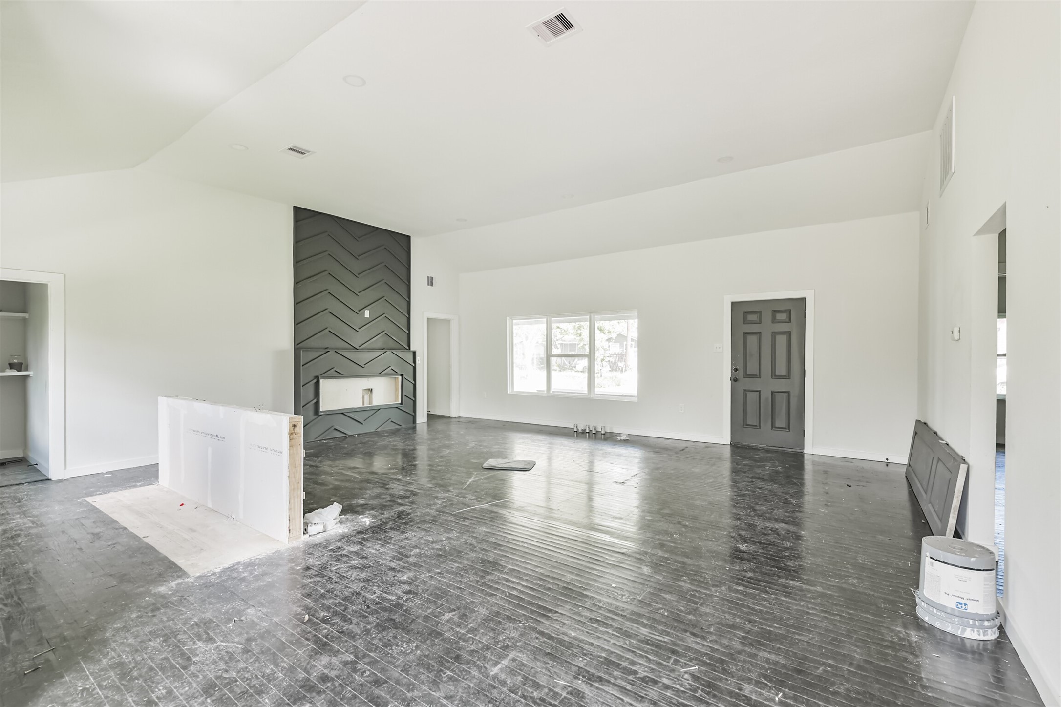 Spacious living area with high ceilings and large windows, featuring a modern accent wall with a fireplace. The room is bright with a neutral color palette, offering a versatile space for personalization.
