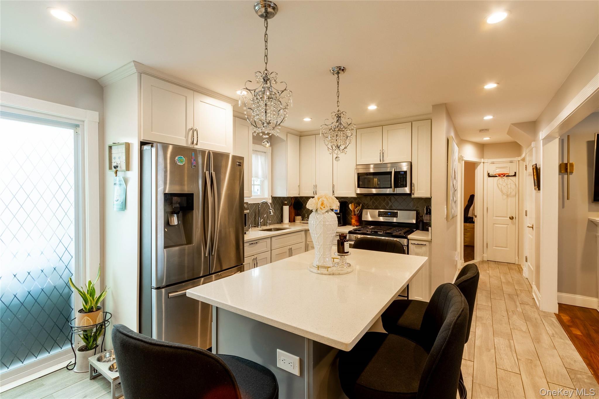 151 Cheltenham Road West Babylon, NY 11704 - Photo 17 of 42 Modern kitchen featuring white shaker cabinetry, stainless steel appliances, a white island countertop, crystal chandeliers, and light wood-finish flooring