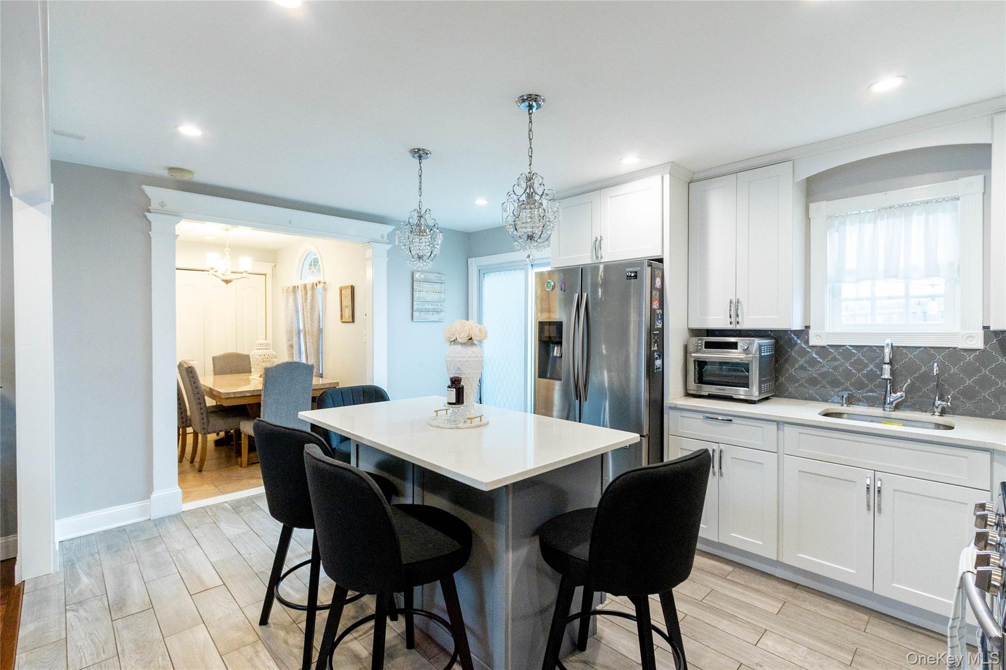 151 Cheltenham Road West Babylon, NY 11704 - Photo 19 of 42 Kitchen featuring a central island with countertop seating, white shaker cabinetry, stainless steel appliances, and a gray arabesque tile backsplash