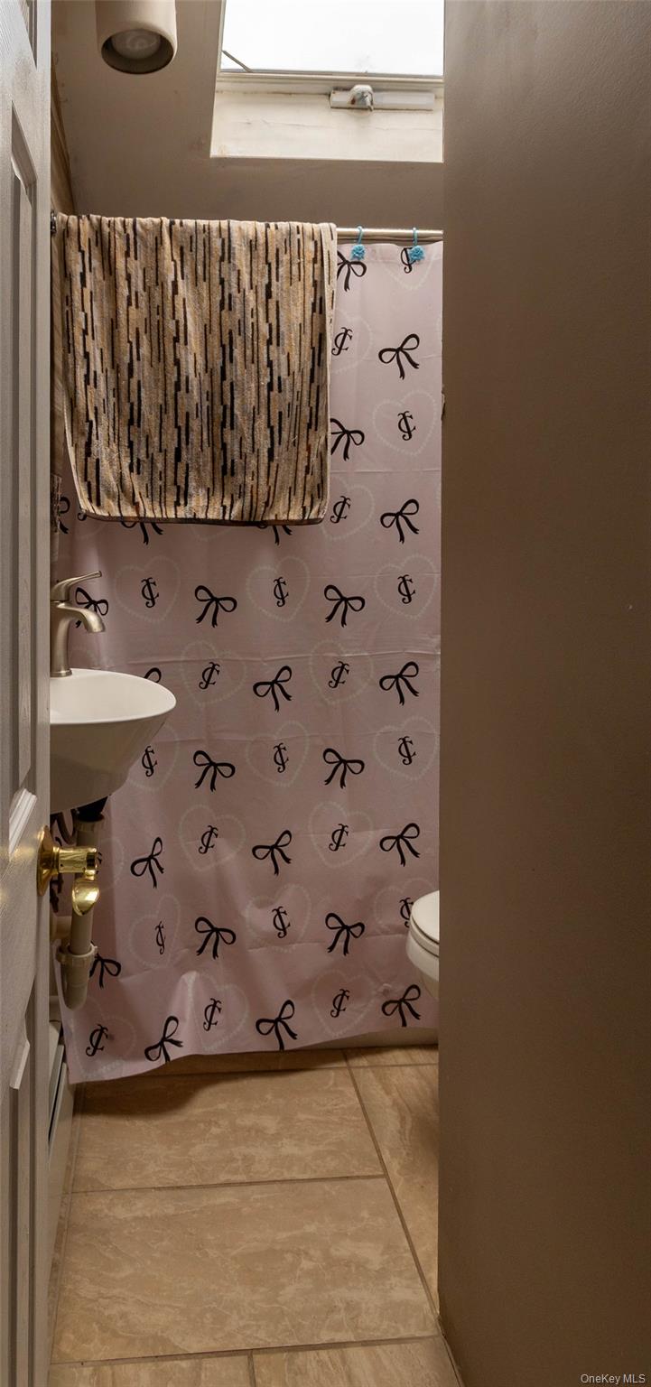 151 Cheltenham Road West Babylon, NY 11704 - Photo 35 of 42 Bathroom featuring a skylight, pedestal sink with single-handle faucet, and tile flooring