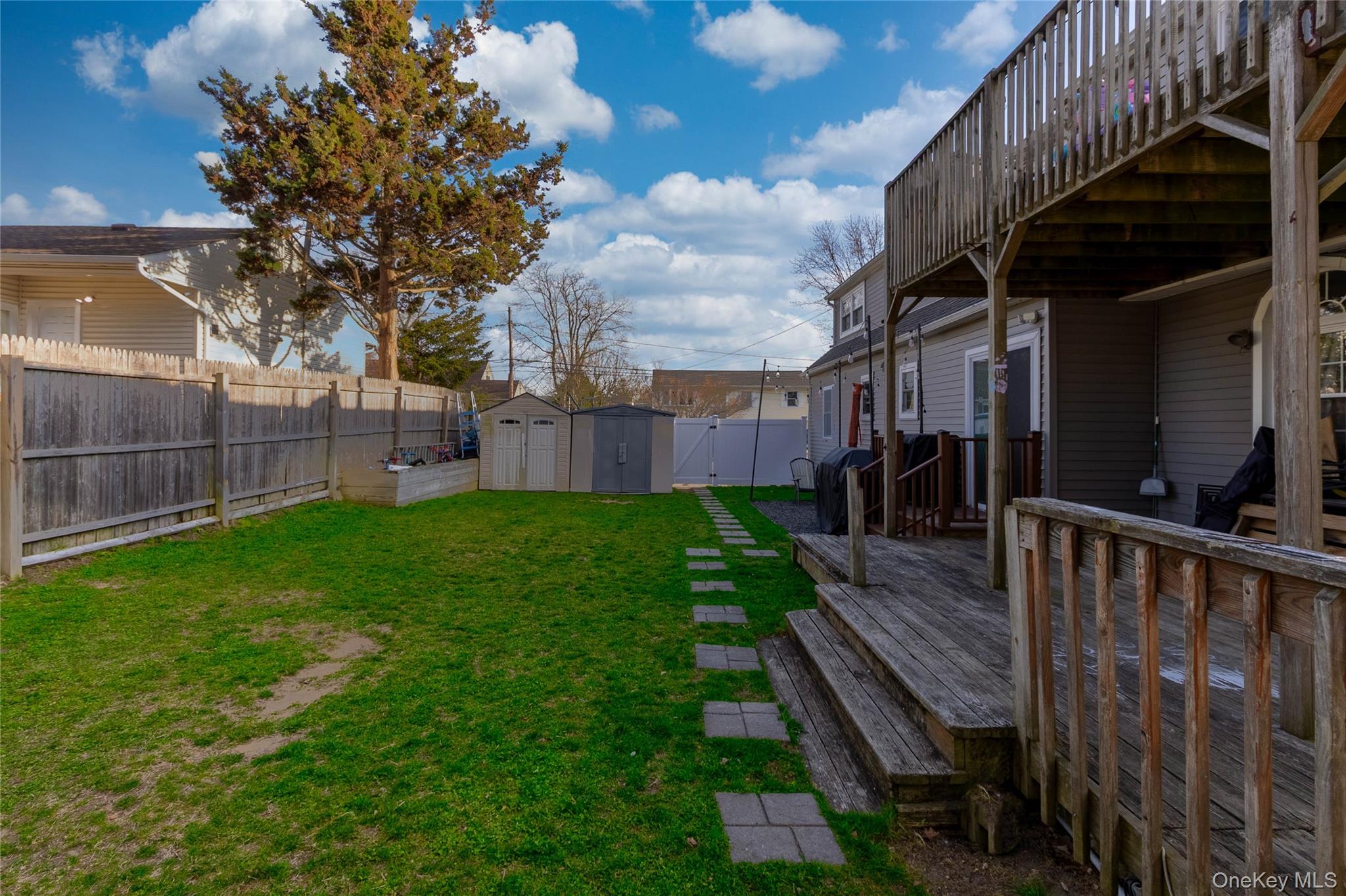 151 Cheltenham Road West Babylon, NY 11704 - Photo 10 of 12 The property features a fenced backyard with a lawn, a stone path, and two storage sheds