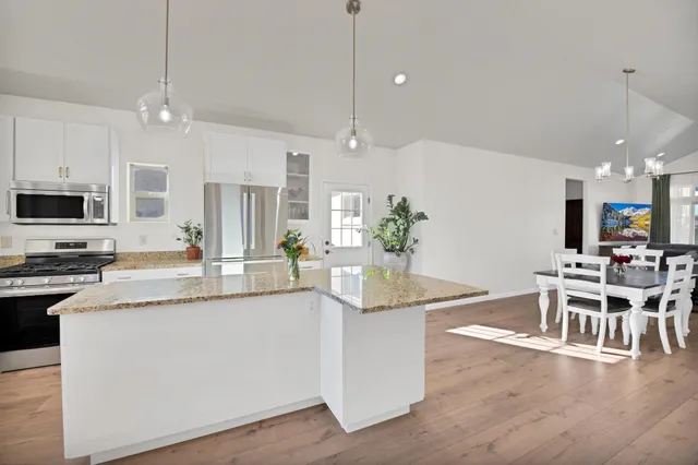 a kitchen with stainless steel appliances kitchen island granite countertop a dining table chairs and white cabinets