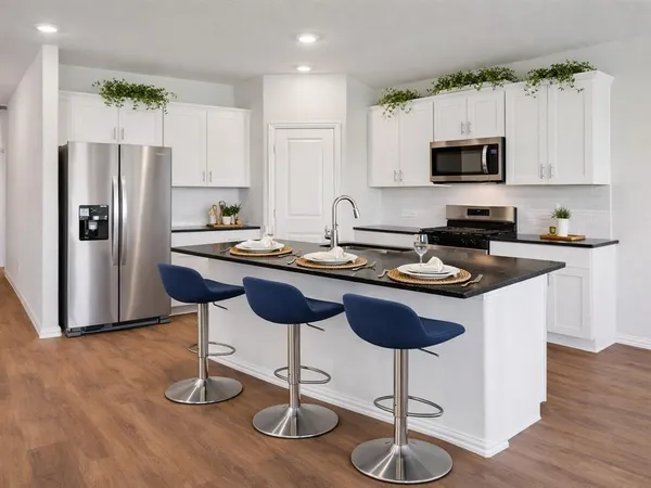 a kitchen with stainless steel appliances granite countertop a stove a sink a refrigerator a microwave a dining table and chairs with wooden floor