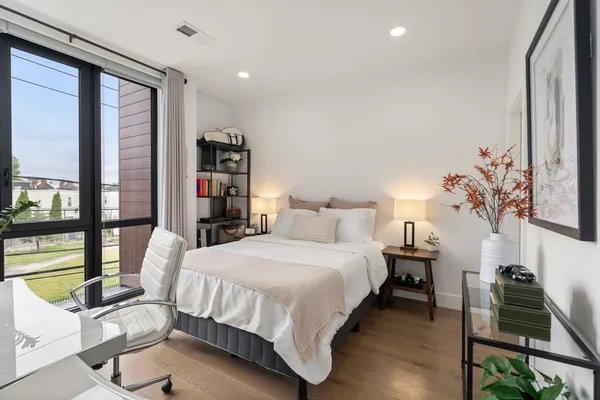a bedroom with a bed table flowerpot and a window
