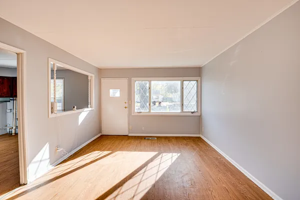 a view of an empty room with wooden floor and a window