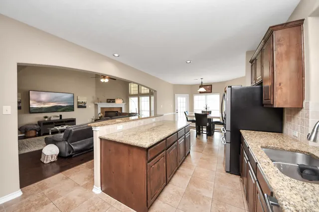 a kitchen with stainless steel appliances granite countertop a refrigerator a stove a sink a dining table and chairs with wooden floor