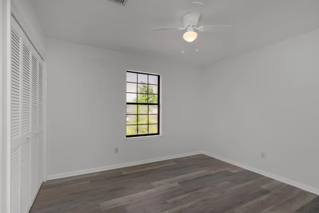 an empty room with wooden floor closet and windows