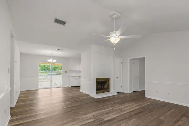 an empty room with wooden floor a chandelier fan and windows