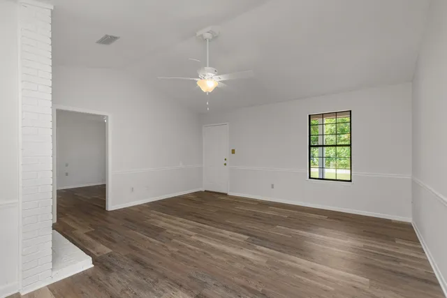 an empty room with wooden floor chandelier fan and windows