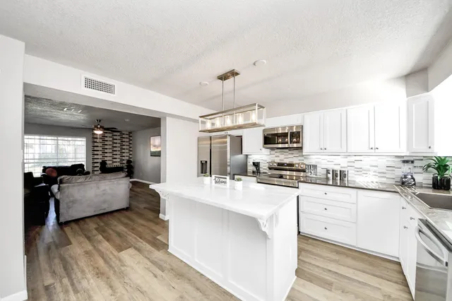 a kitchen with stainless steel appliances granite countertop a stove top oven a sink dishwasher and white cabinets with wooden floor