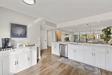 a large white kitchen with a sink dishwasher a stove and white cabinets with wooden floor