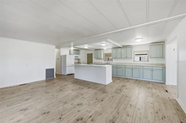 a large white kitchen with kitchen island a sink wooden floor and a refrigerator
