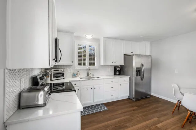 a kitchen with stainless steel appliances a stove a sink a refrigerator white cabinets and wooden floor