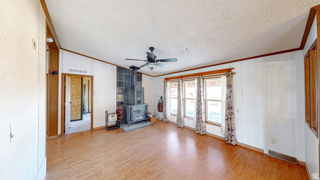 718 South State Street Genola, UT 84655 - Photo 5 of 19 Spacious room featuring wood-finish flooring, a wood stove on a stone hearth, and a ceiling fan
