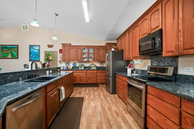 a large kitchen with stainless steel appliances granite countertop a stove a sink dishwasher and a microwave oven with large wooden cabinets