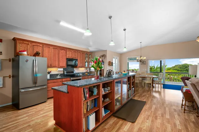 a kitchen with stainless steel appliances granite countertop a refrigerator a sink dishwasher a stove and a dining table with wooden floor