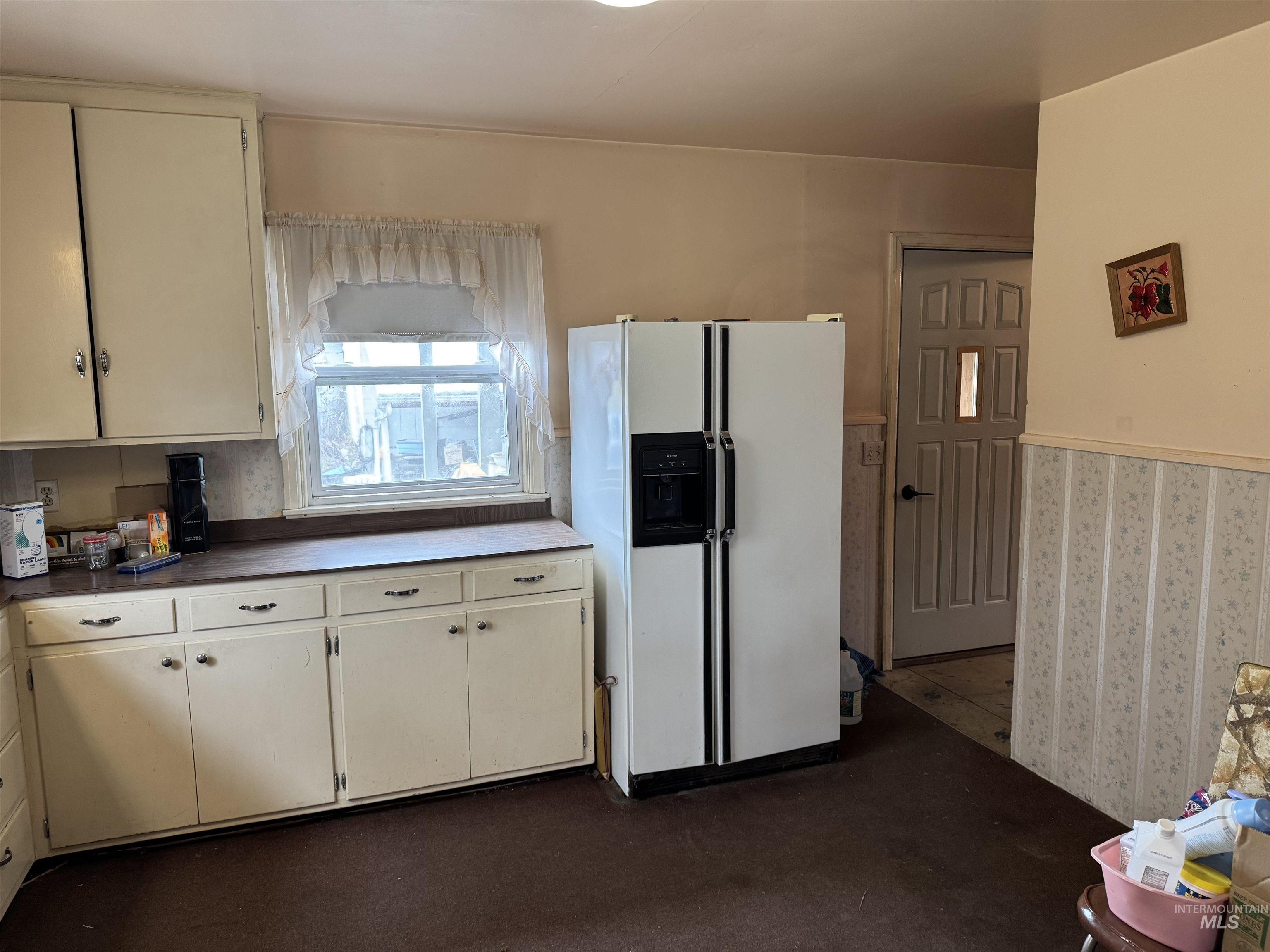 1109 3rd Street Kamiah, ID 83536 - Photo 7 of 17 Kitchen featuring white fridge with ice dispenser, dark countertops, cream cabinetry, and dark carpet