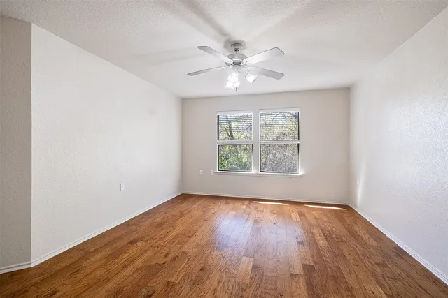 an empty room with wooden floor chandelier fan and windows