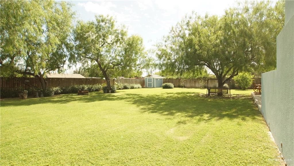 414 Ric Mar Street Edinburg, TX 78541 - Photo 10 of 36 Spacious backyard featuring a manicured lawn, established shade trees, a perimeter wood fence, and a light blue storage shed