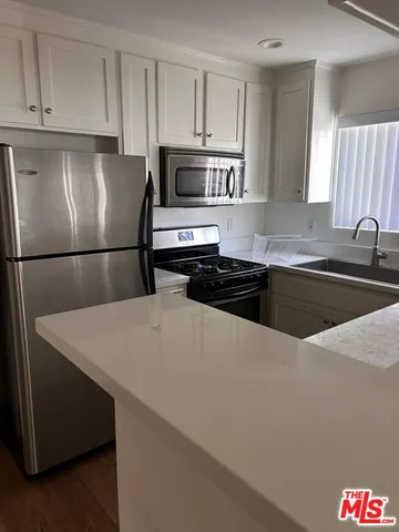 a kitchen with stainless steel appliances a refrigerator a sink a stove and white cabinets