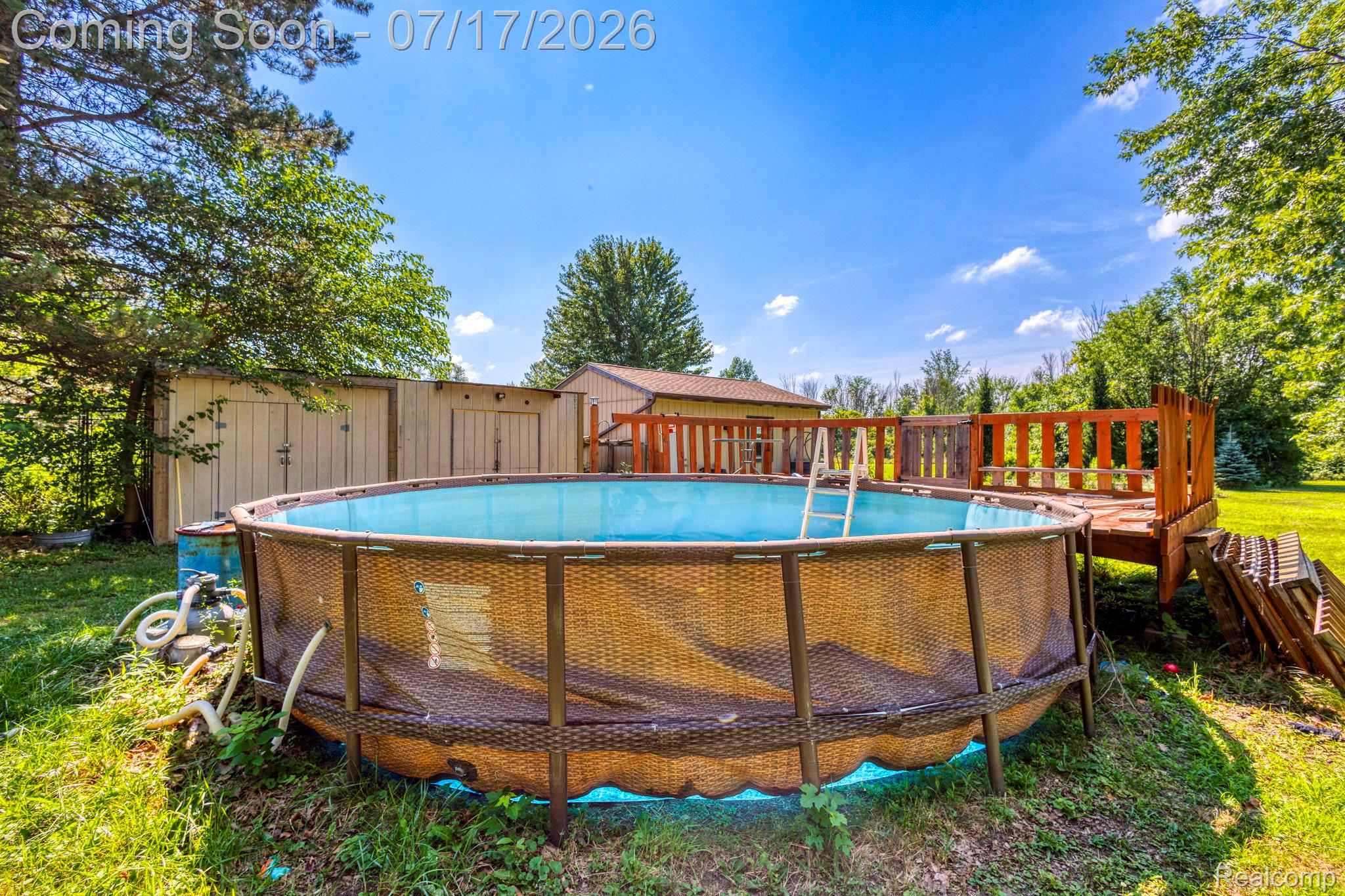 9805 Dolan Road Columbus, MI 48063 - Photo 28 of 39 Above-ground pool with a surrounding wood deck, accompanied by two storage sheds