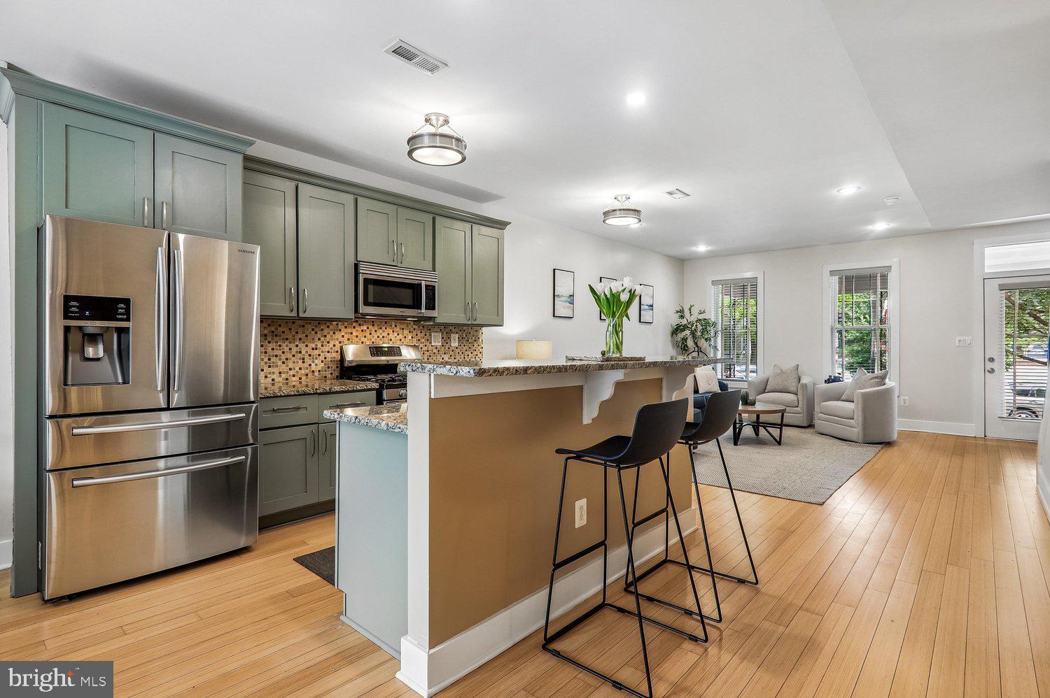 911 L Street Northeast Washington, DC 20002 - Photo 9 of 48 a kitchen with stainless steel appliances kitchen island granite countertop a refrigerator a stove a sink dishwasher and a dining table with wooden floor