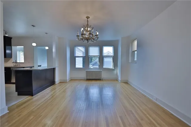an empty room with wooden floor chandelier and windows