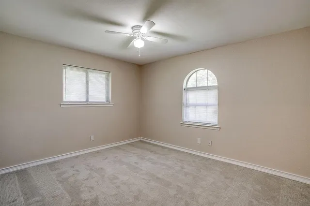 an empty room with a chandelier fan and windows