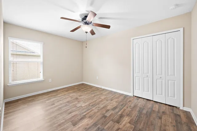an empty room with wooden floor fan and windows