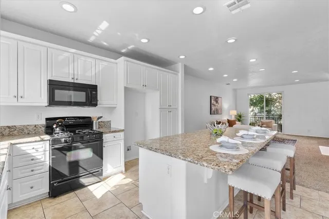 a kitchen with kitchen island granite countertop a stove a sink a microwave a dining table and chairs