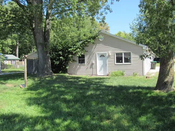 a backyard of a house with plants and large tree