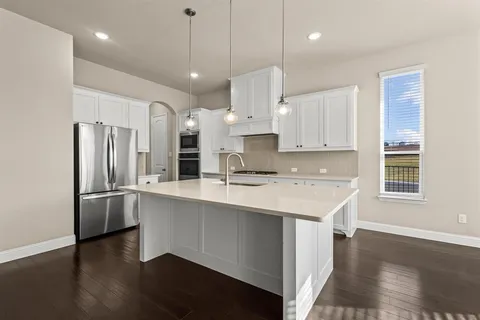 a kitchen with stainless steel appliances granite countertop a refrigerator a sink dishwasher a stove and white cabinets with wooden floor