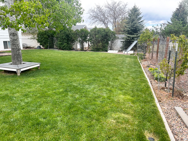 570 250 East Parowan, UT 84761 - Photo 27 of 27 Expansive lawn area featuring a mature tree with built-in bench seating, bordered by a planted garden bed and natural fencing