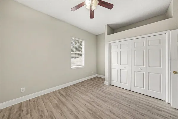 an empty room with wooden floor chandelier fan and windows