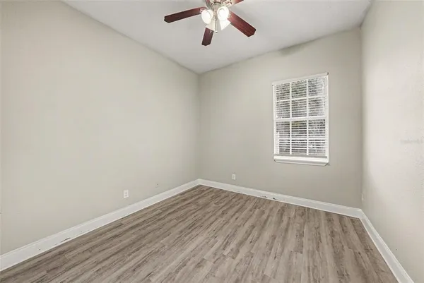 an empty room with wooden floor chandelier fan and windows