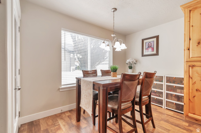 13038 Tower Ridge Drive Riverton, UT 84096 - Photo 10 of 30 Dining area featuring wood-finish flooring, a contemporary chandelier, and a large window with privacy blinds