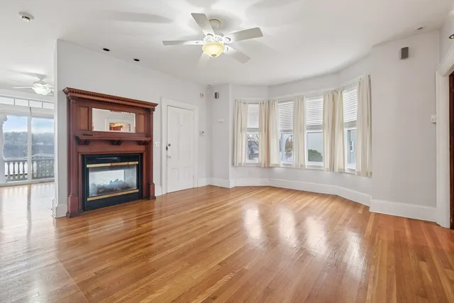 a view of an empty room with wooden floor fireplace and a window
