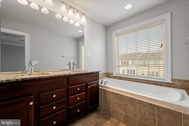 a spacious bathroom with a granite countertop double vanity sink large mirror and a bathtub