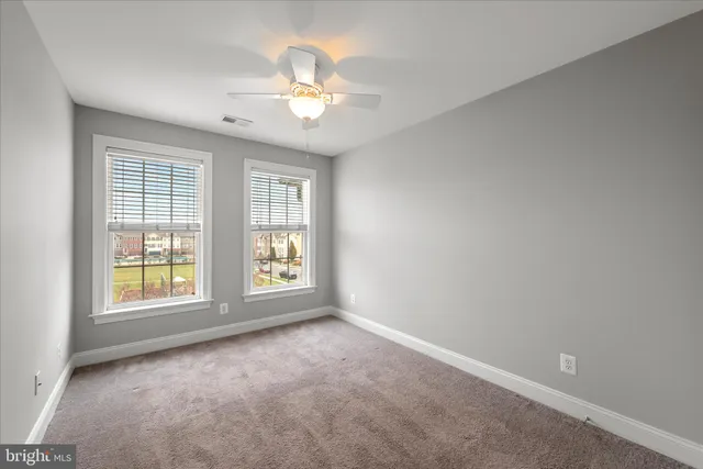 an empty room with chandelier fan and windows
